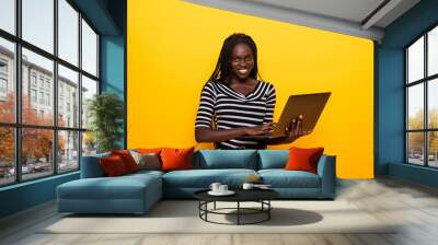 Young african positive woman using laptop and smiling isolated over yellow background Wall mural